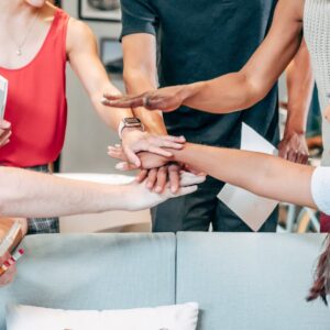 A diverse group of coworkers uniting hands in an office setting, symbolizing teamwork and collaboration.